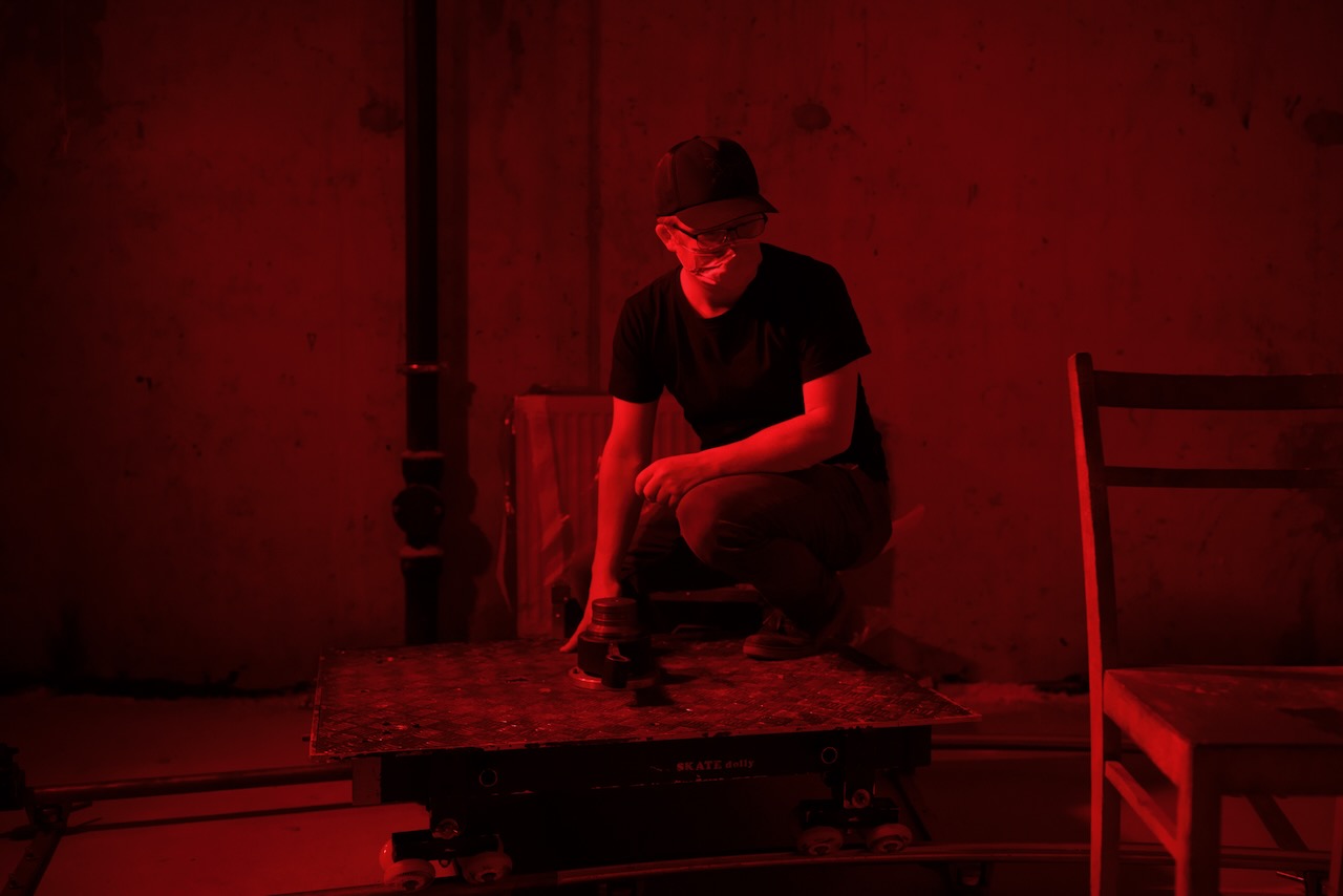 A crew member on a skate dolly under red light.