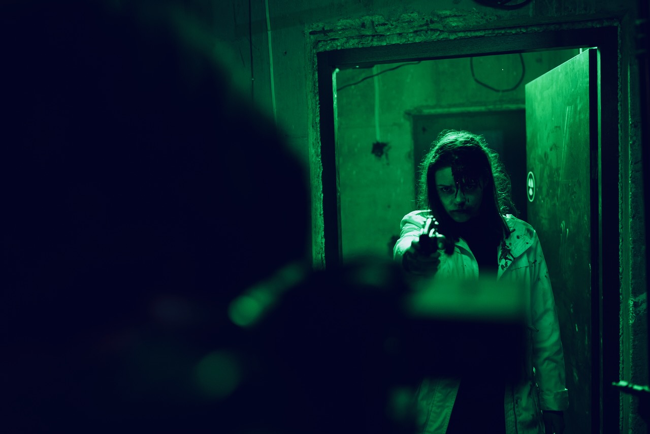 A figure in a doorway aiming a gun, lit green.