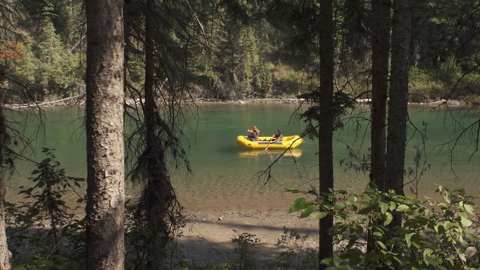 A yellow raft on a green mountain river, seen through trees.