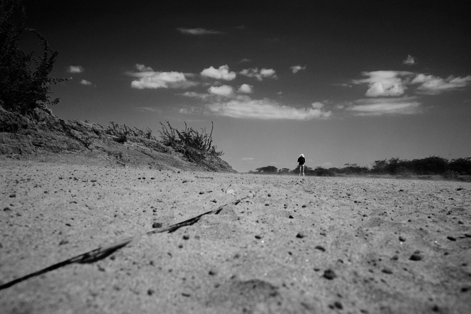A figure walking a dry, sandy riverbed.