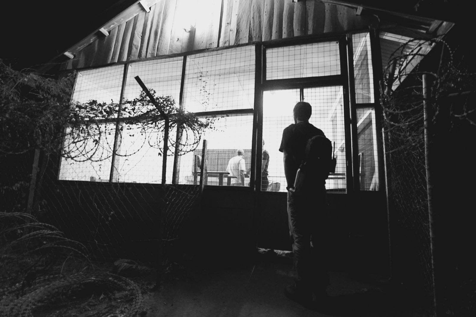 A person standing at the lit doorway of a screened building at night.