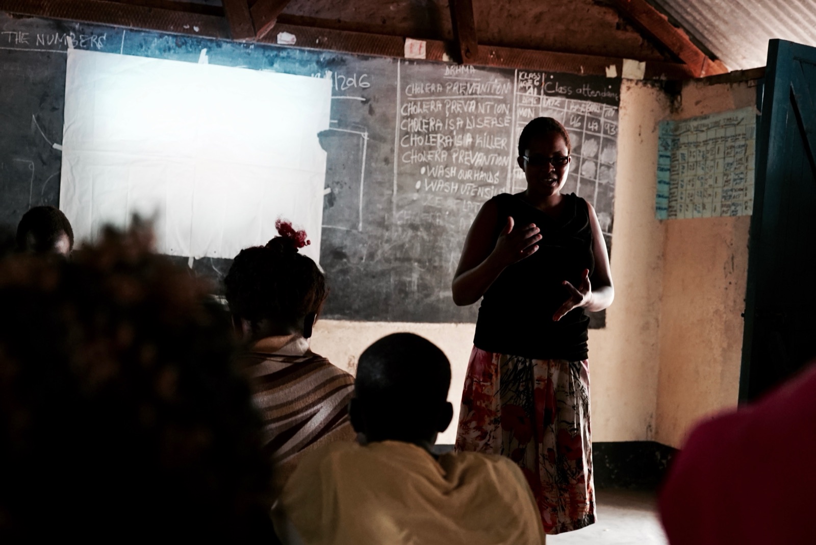A woman teaching a cholera-prevention class at a chalkboard.